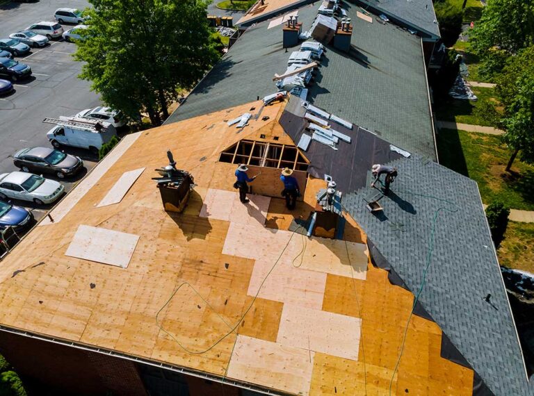 A person safely inspecting asphalt shingles and roof flashing on a residential home under partly cloudy skies.